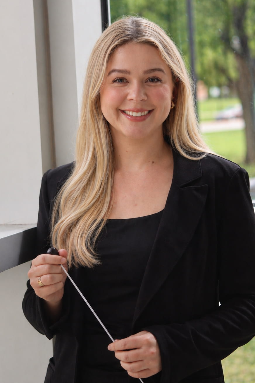Headshot of a white person with long blonde hair in a black under a black blazer.