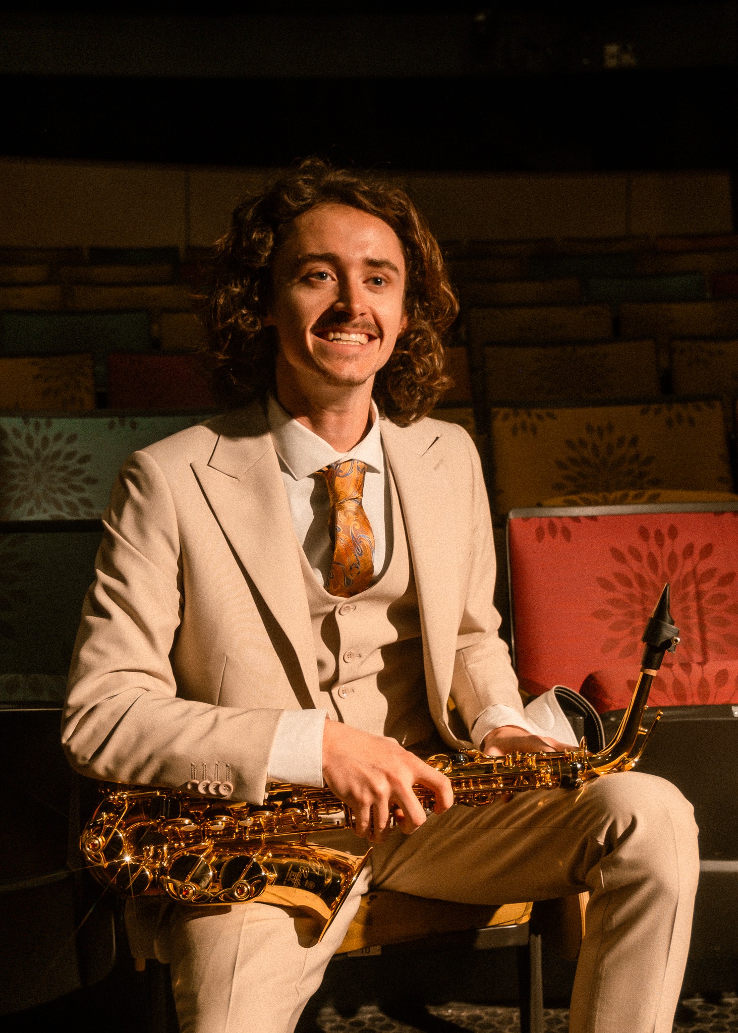 Cameron Montgomery, dressed in a tan suit, holds an alto saxophone in his professional headshot
