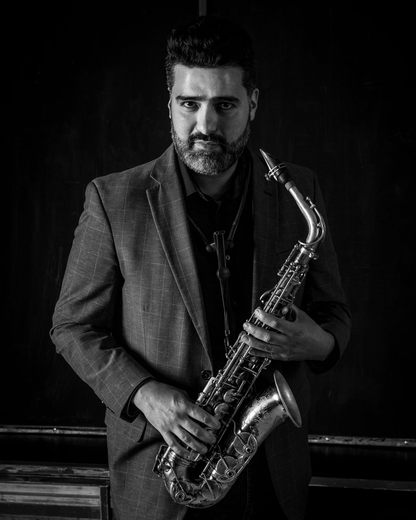 Mario Montes Lara, dressed in a suit, holds an alto saxophone in his professional headshot