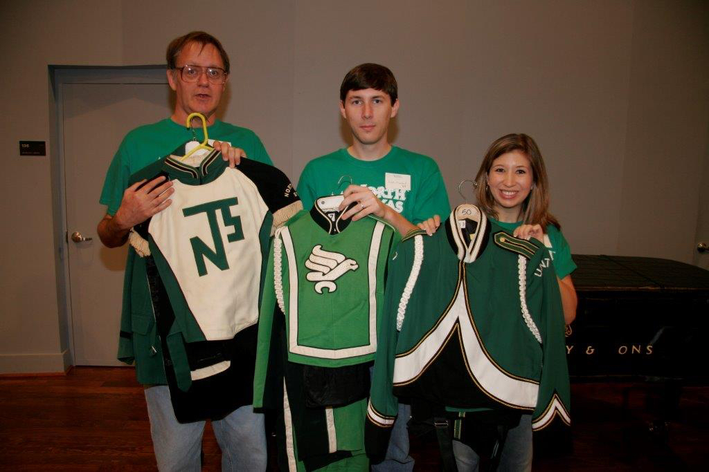 Three Green Brigade Alumni posing with their respective versions of the uniform from past generations