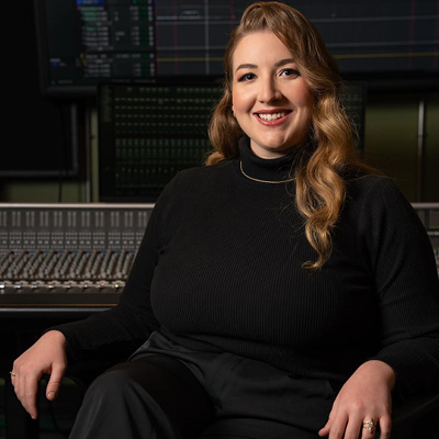Ms. Neivandt-Brown is sitting in a recording studio wearing black with a small necklace. She is smiling looking into the camera.