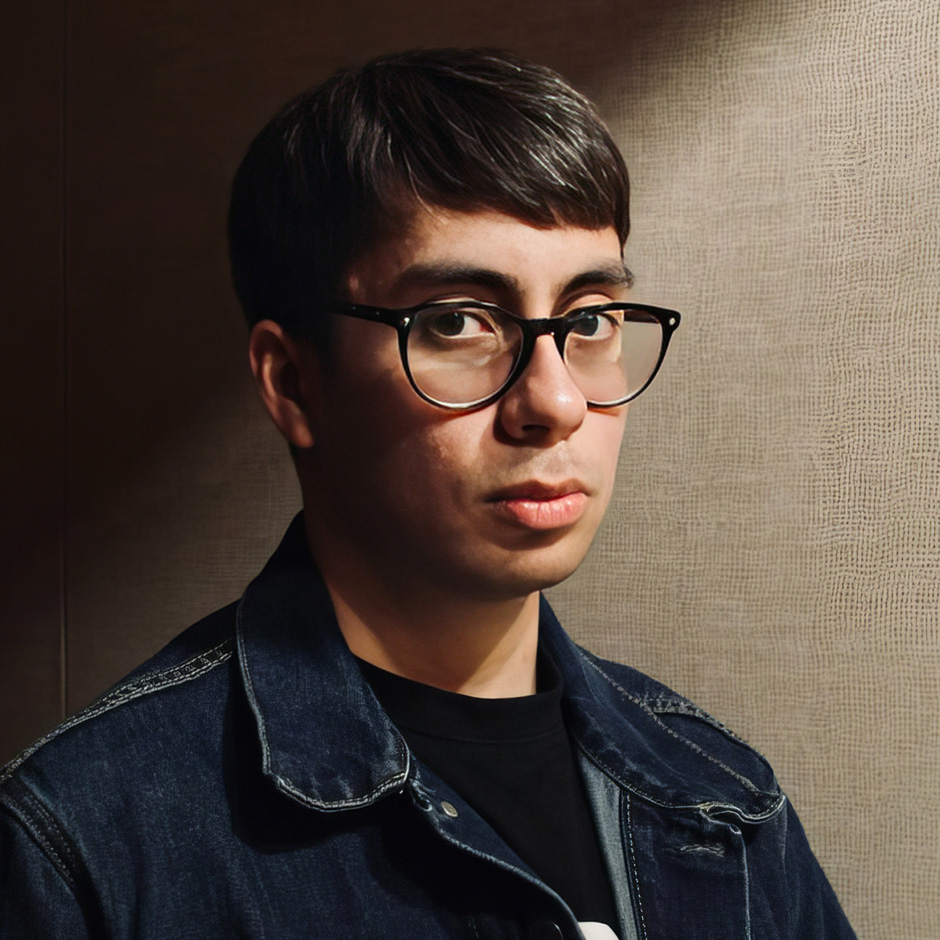 Ricardo is wearing a black tee shirt with a blue jacket. His hair is dark and his eyeglasses are black-rimmed.