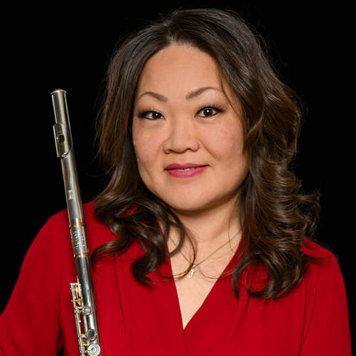 Julee Kim Walker (DMA ‘13), female with shoulder-length brown hair (curled), brown eyes, wearing a red shirt, holding a flute.