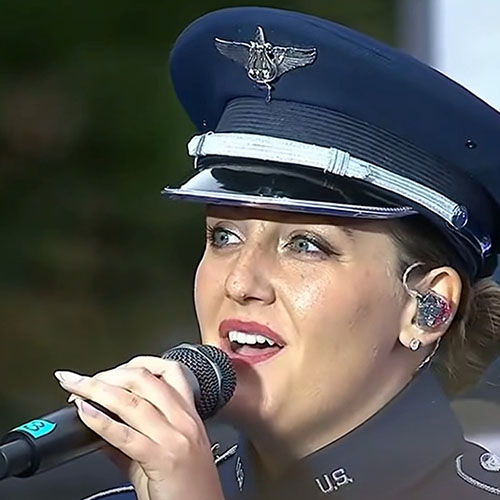 Kayla Highsmith Richardson wearing a military uniform and holding a microphone, singing live.